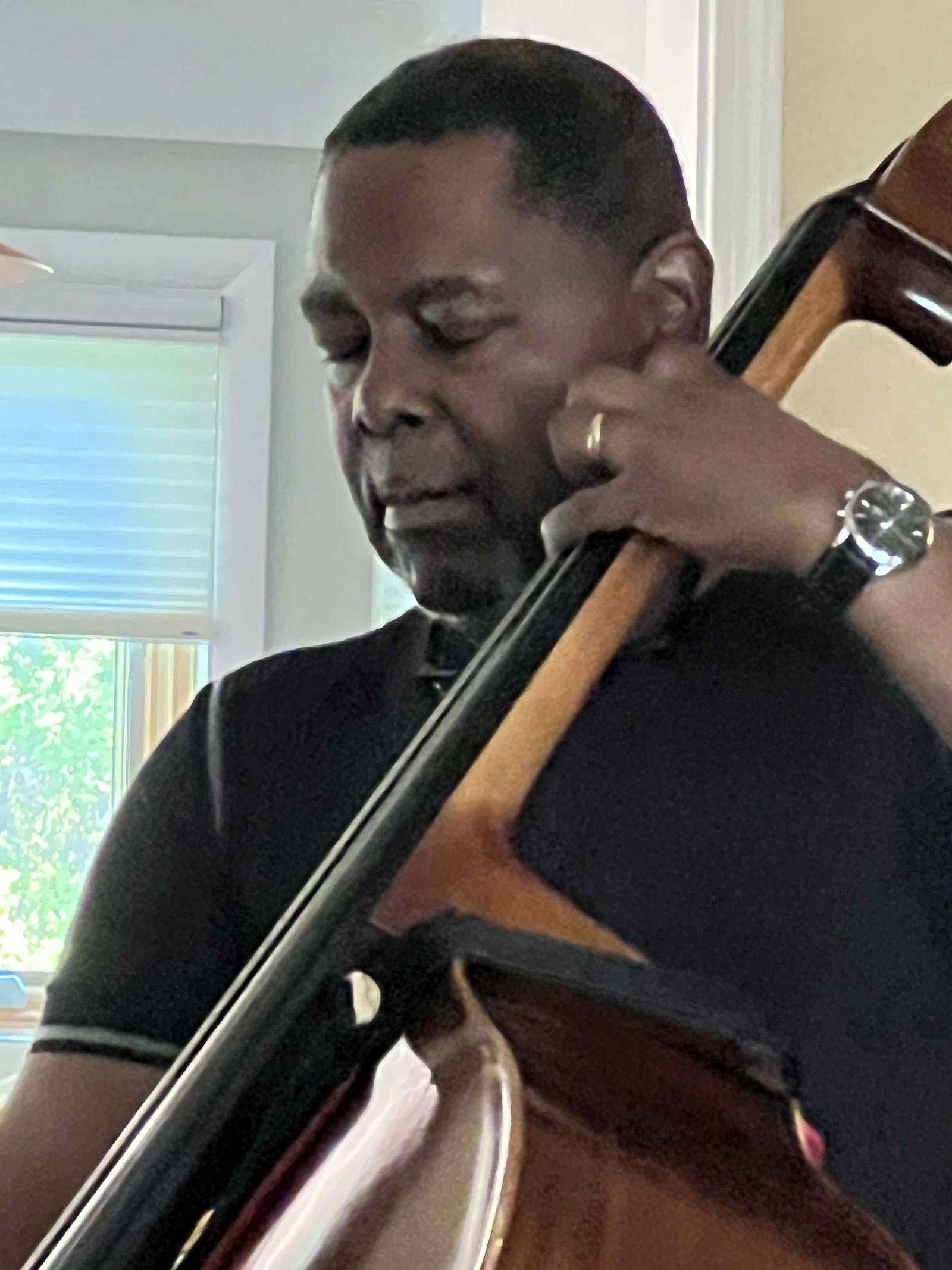 A man holding a large cello on the right side of his body. He has his eyes closed and he's playing