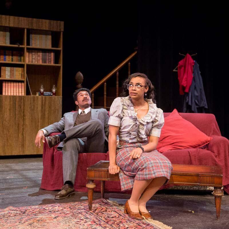 Two people sitting on a couch on a theatre stage