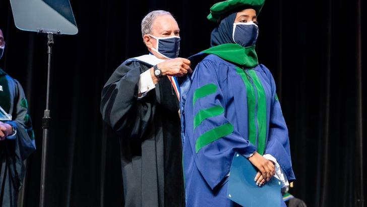 Michael Bloomberg placing graduation hood on student