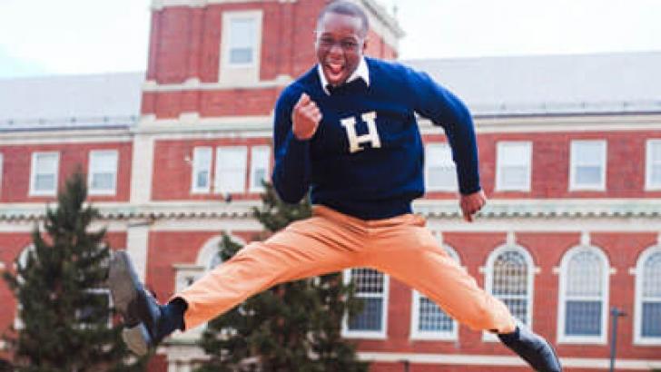 Student with Howard sweater jumping in front of Howard building