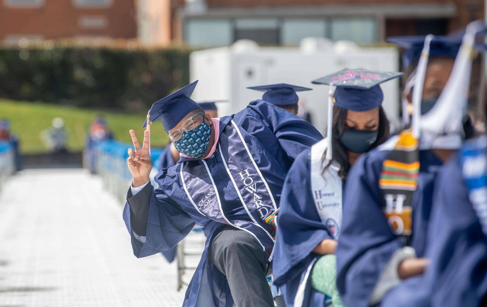 Student in seat at graduation throwing up a peace sign