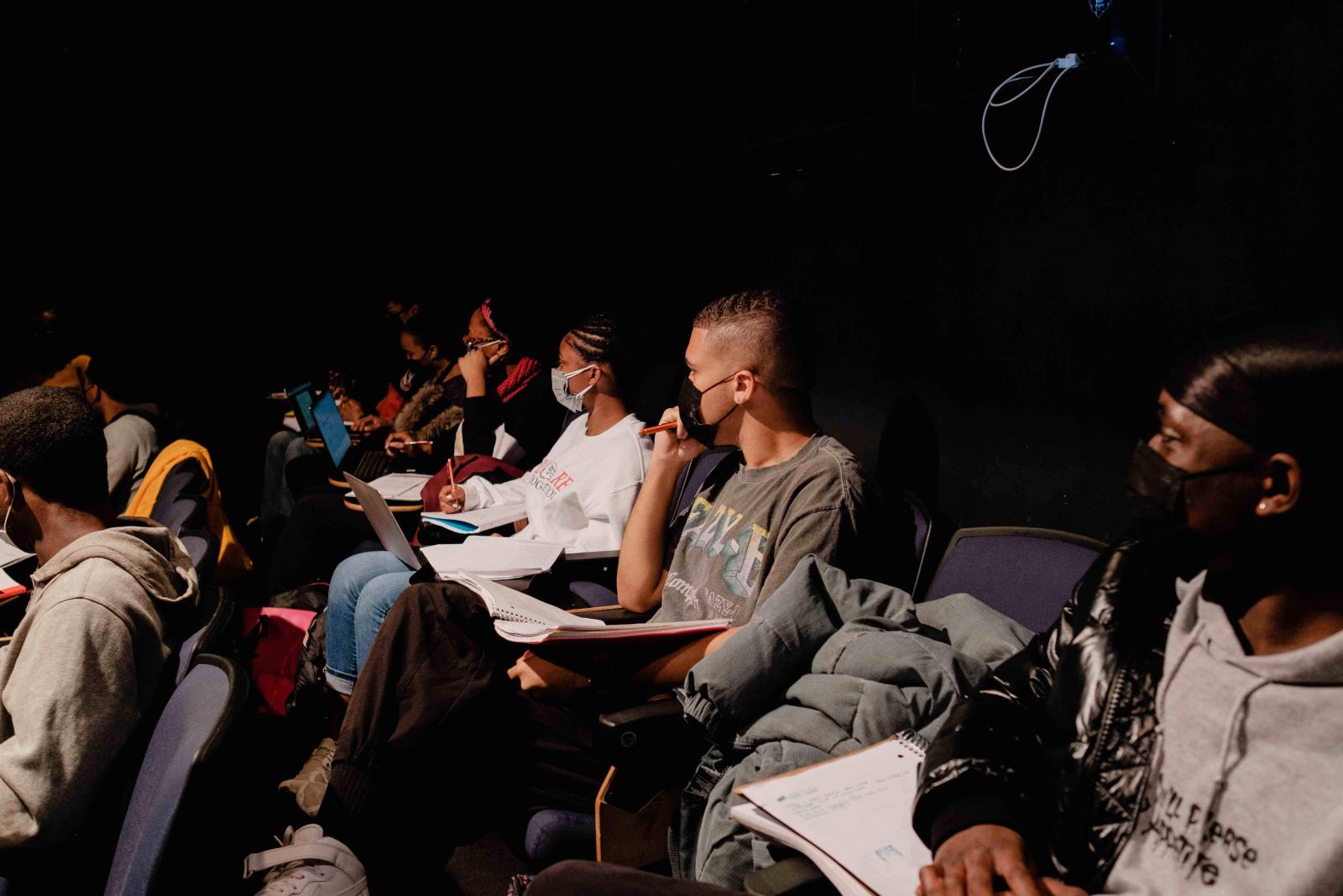 students sitting in a dark theater taking notes