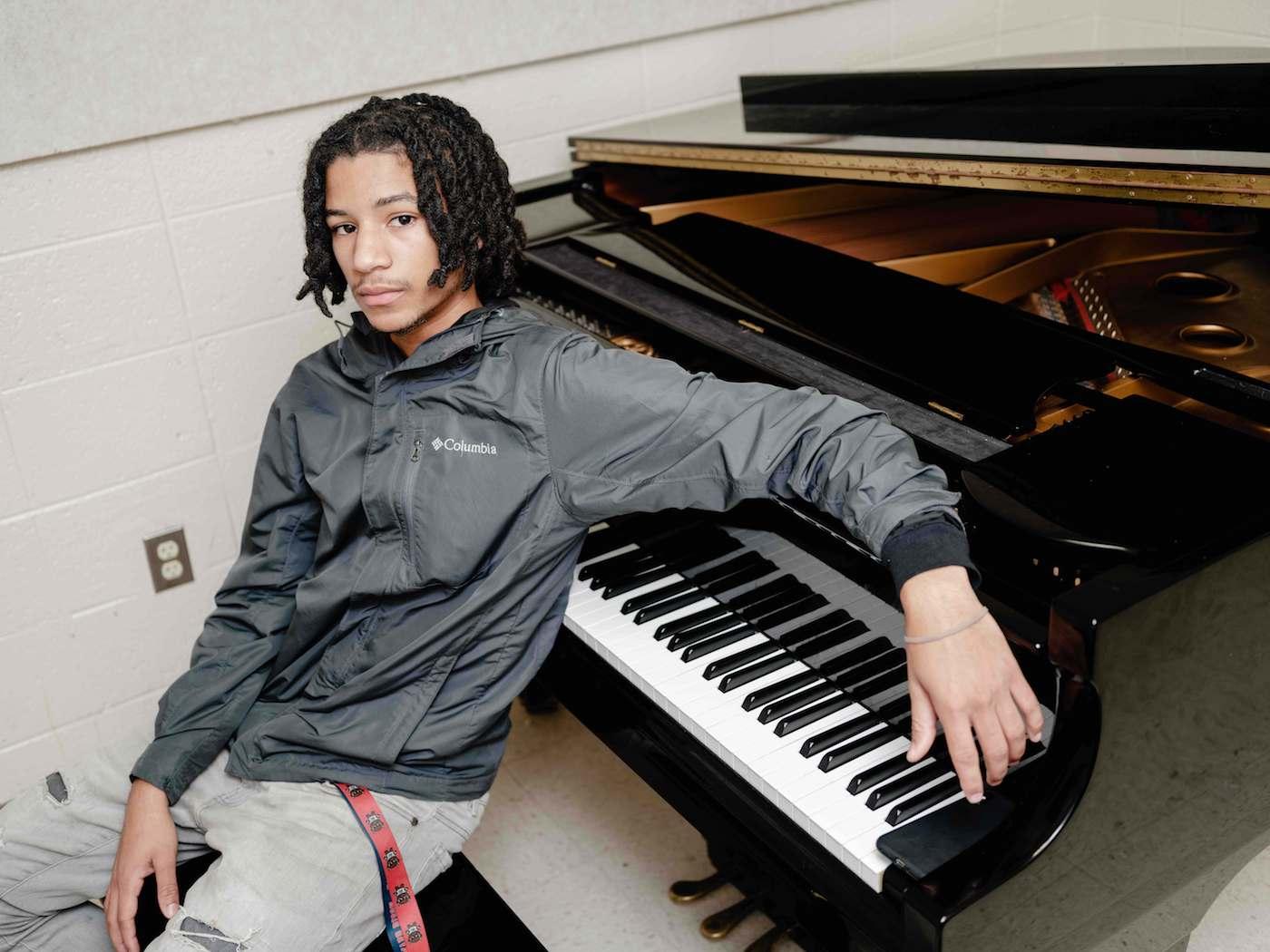 male student leaning against a piano