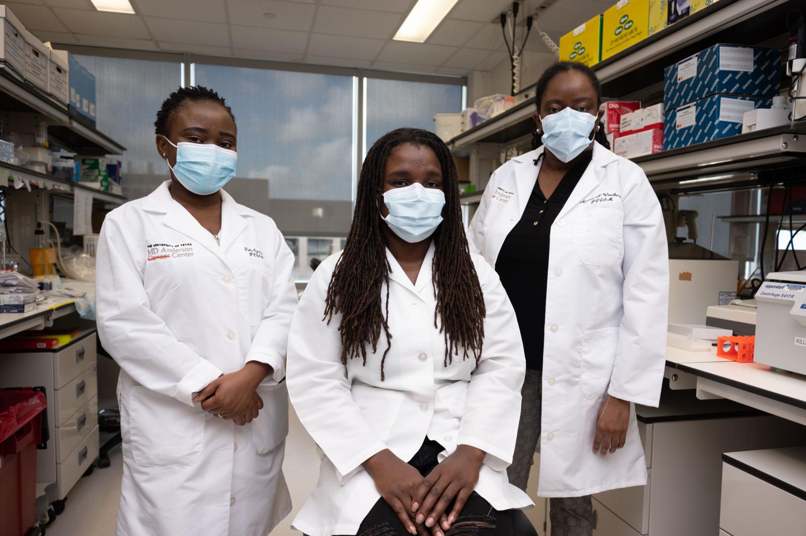 three researchers in white coats and masks