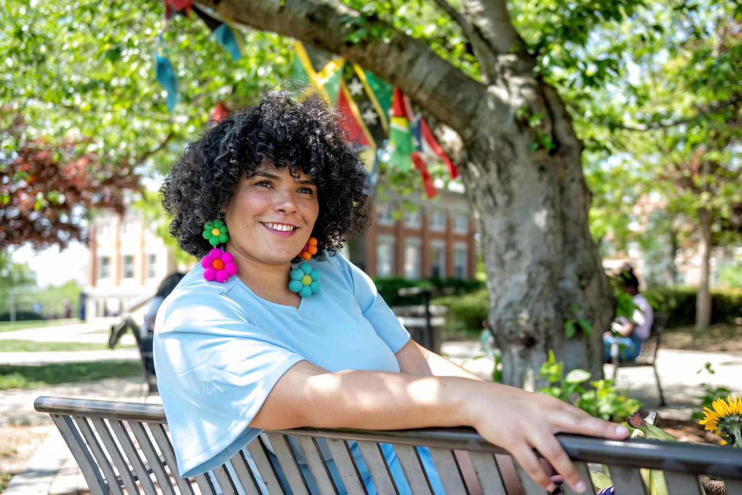 Natalie Munoz sitting on bench outside under Caribbean flags