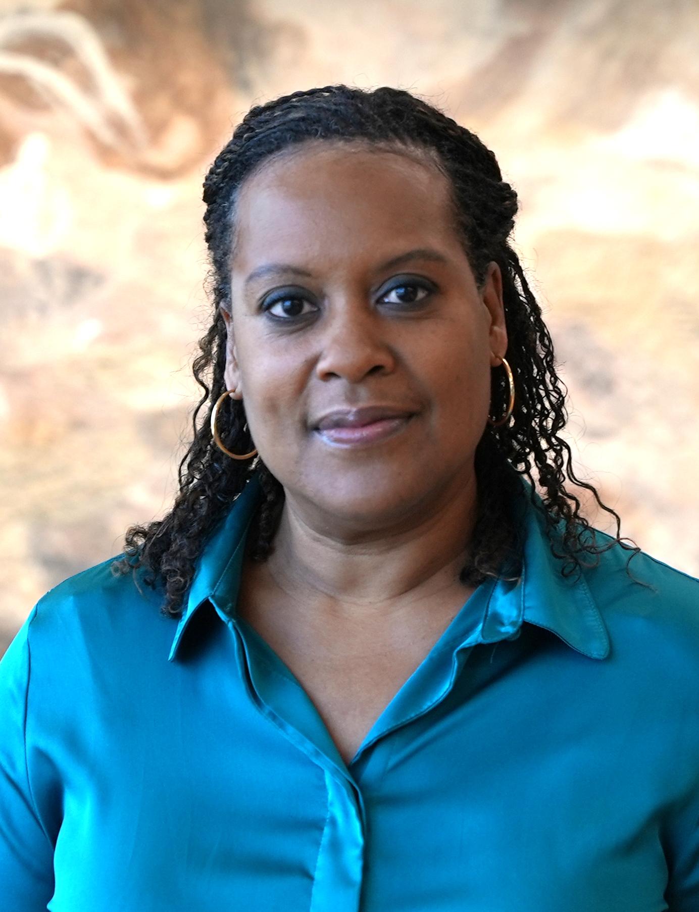 Robin V. Harris poses for a professional headshot, and wearing a teal blue button up and smiling without showing her teeth.