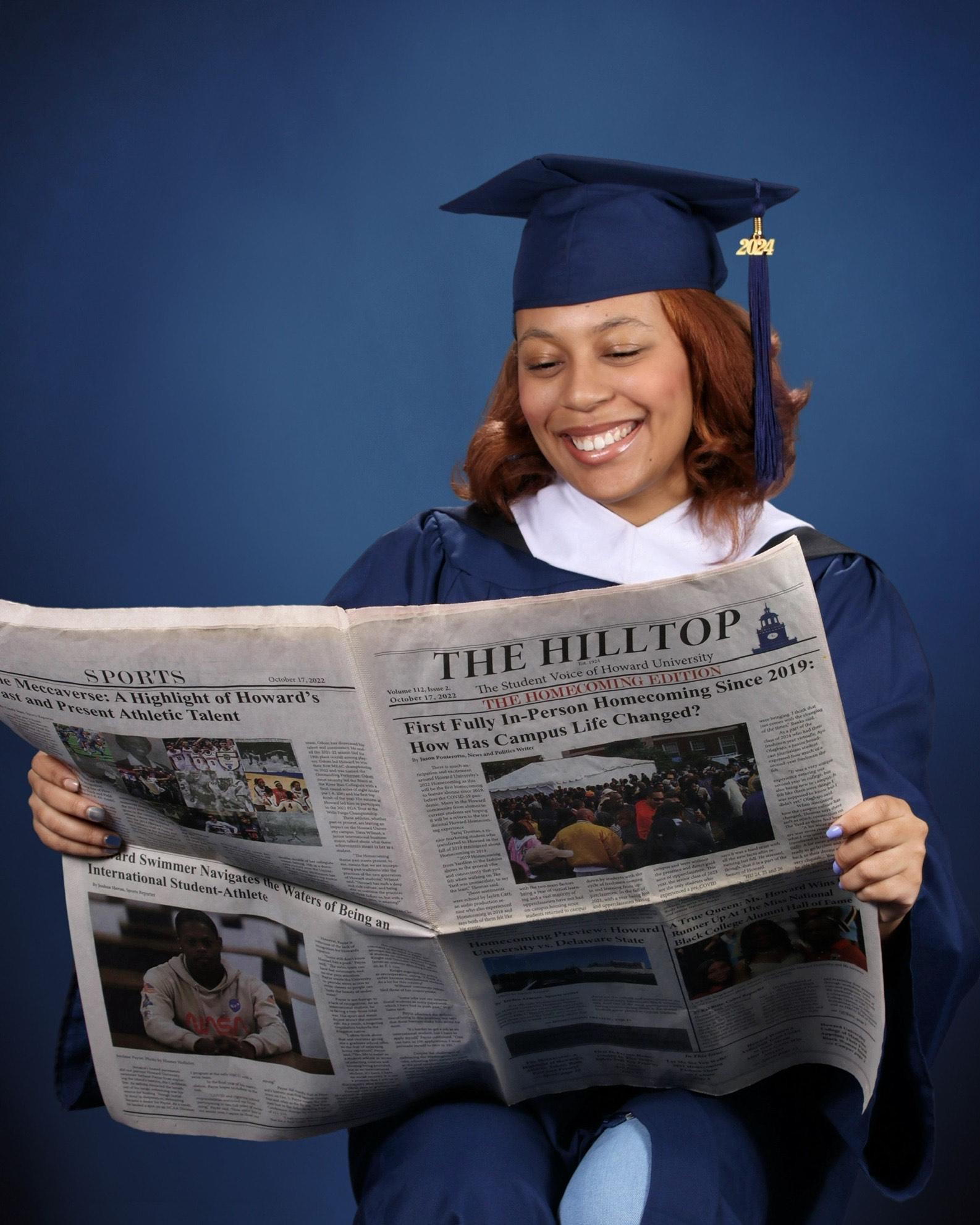 N'dia Webb in cap and gown holding The Hilltop newspaper