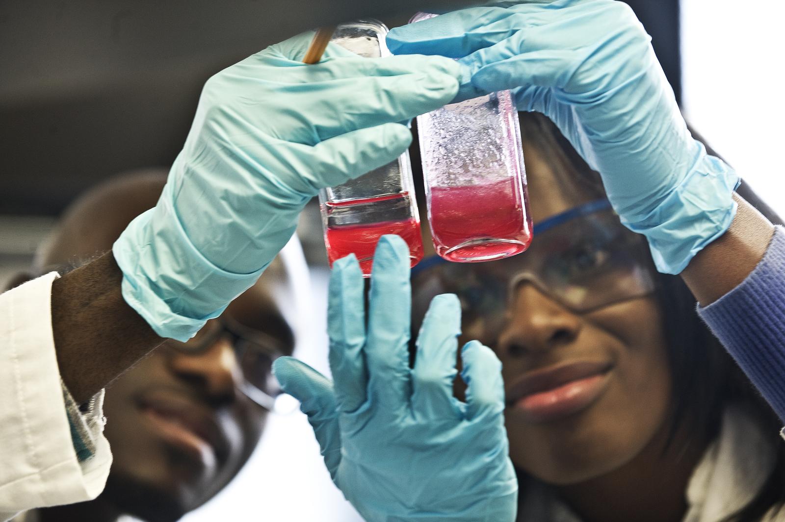 A male researcher and female researcher hold up tubes of fluid.